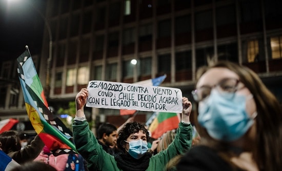 Chilean protester with placard: "25/10/2020: Against wind and covid; Chile decides to finish with the legacy of the dictator"