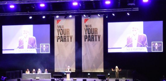 Jeremy Corbyn addresses the Your Party conference hall in front of large screens and banners
