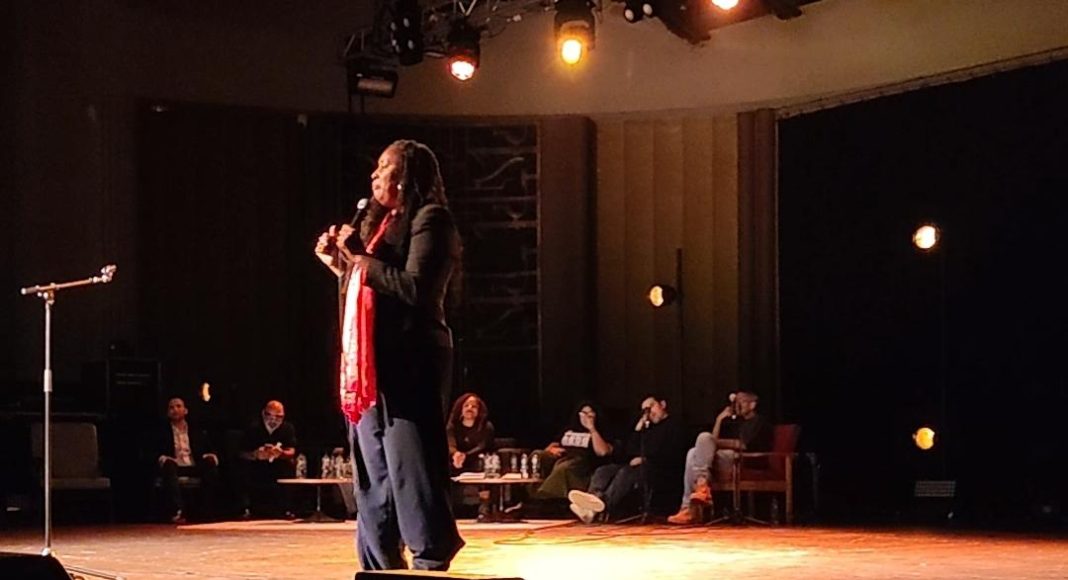 Dawn Butler, Labour MP, addresses the Together Alliance campaign launch on stage. Other speakers watch from sofas and chairs at the back of the stage. (photo: FRFI)