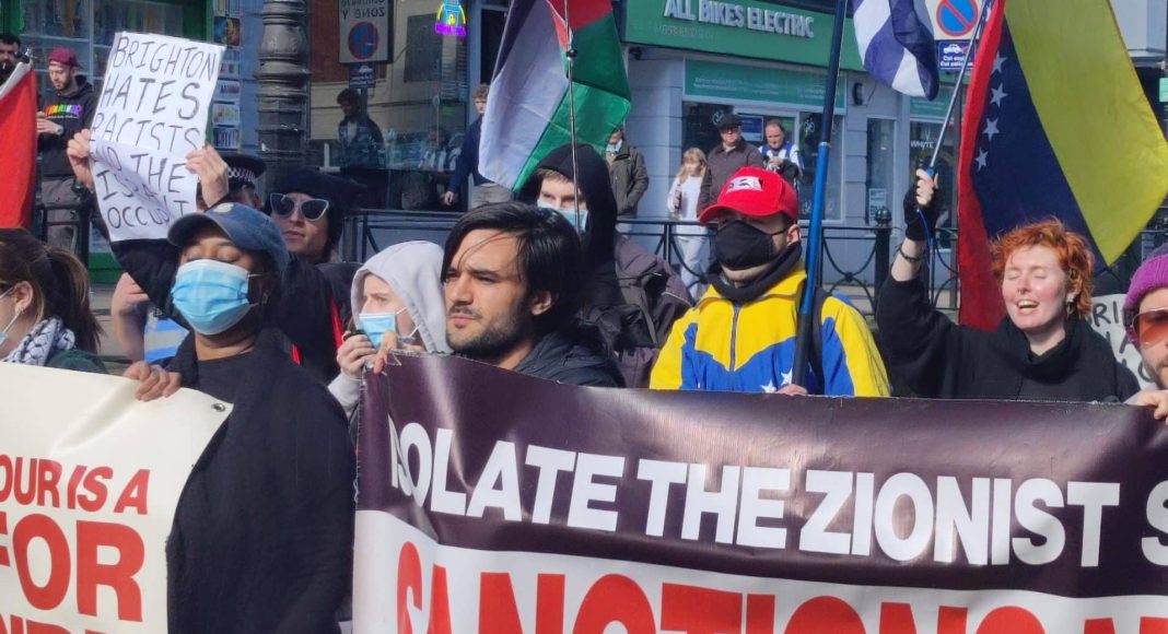 Protesters march down a street waving Palestine, Cuba and Venezuela flags, carrying a banner reading 'isolate the Zionist state - sanctions now'
