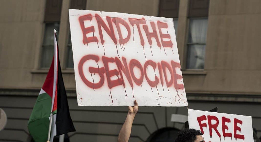 Rally in Melbourne in support of Palestine. Man holds placard reading 'end the genocide' in red lettering (photo: Matt Hrkac/CC BY 2.0)