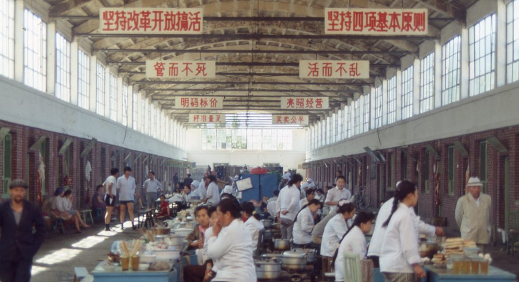 A market in Xinjiang in 1992. The suspended signs read 'Adhere to Reform and Opening up to revitalise the country, keep the Four Cardinal Principles' (Photo: Flickr, fdecomite, CC By 2.0)